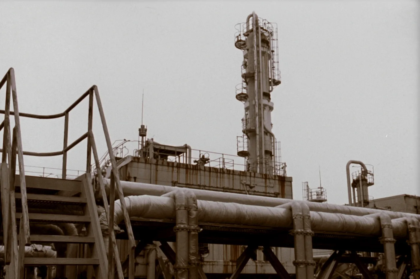 A process plant in daylight: pipe racks, insulated lines and a distillation column under an overcast sky.