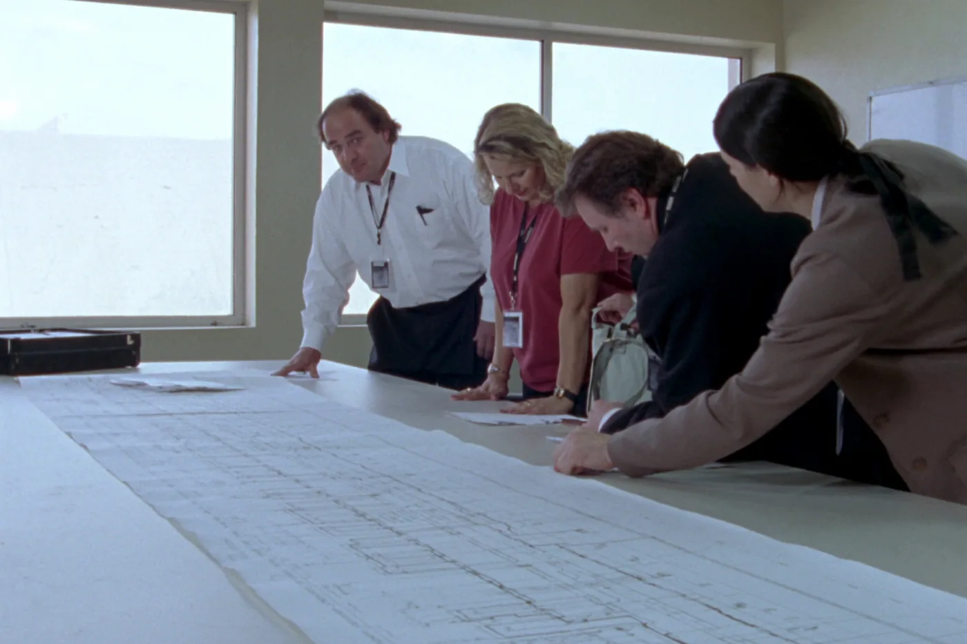 A HAZOP session in a bright meeting room: engineers leaning over a large piping schematic spread across a long table.